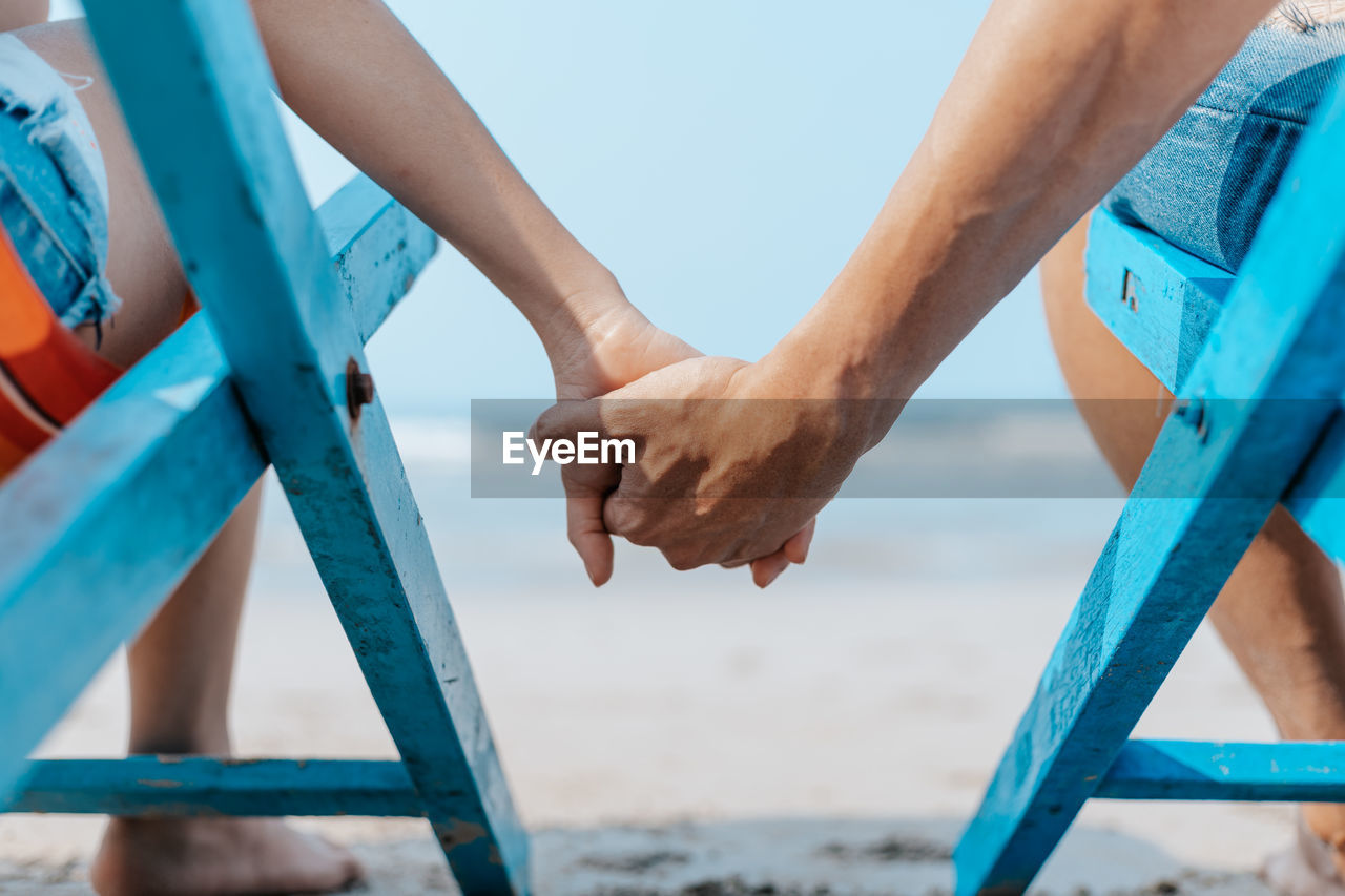 Close-up of couple holding hands at beach