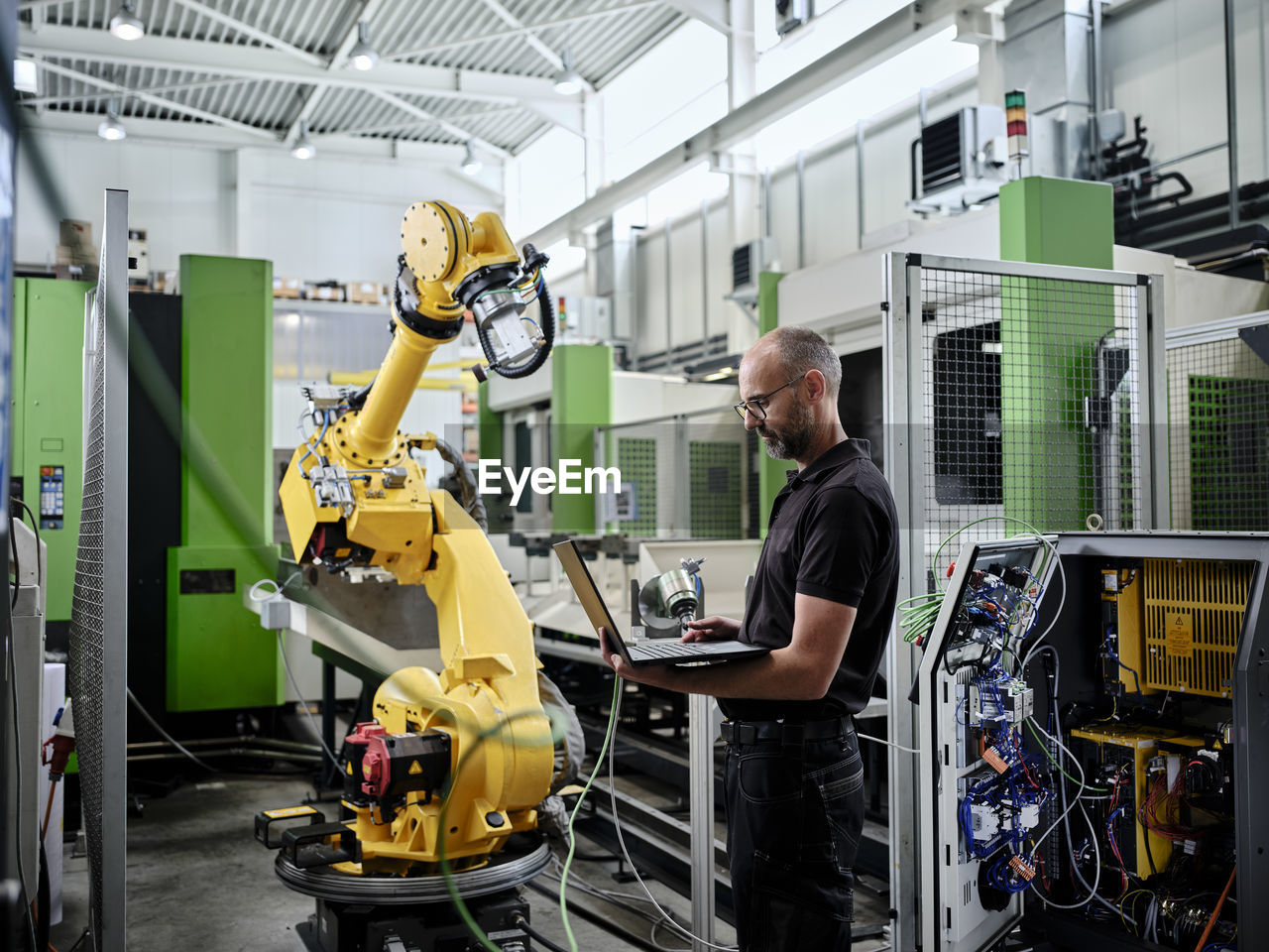 Male engineer using laptop by robotic arm