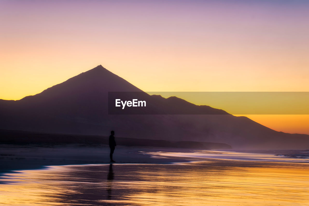 Silhouette person in sea against sky during sunset