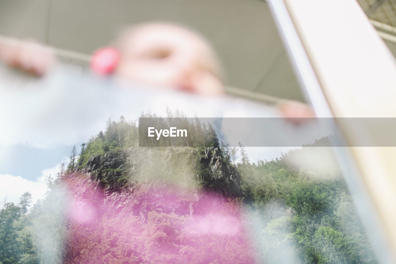 Girl looking through train window with reflection of trees