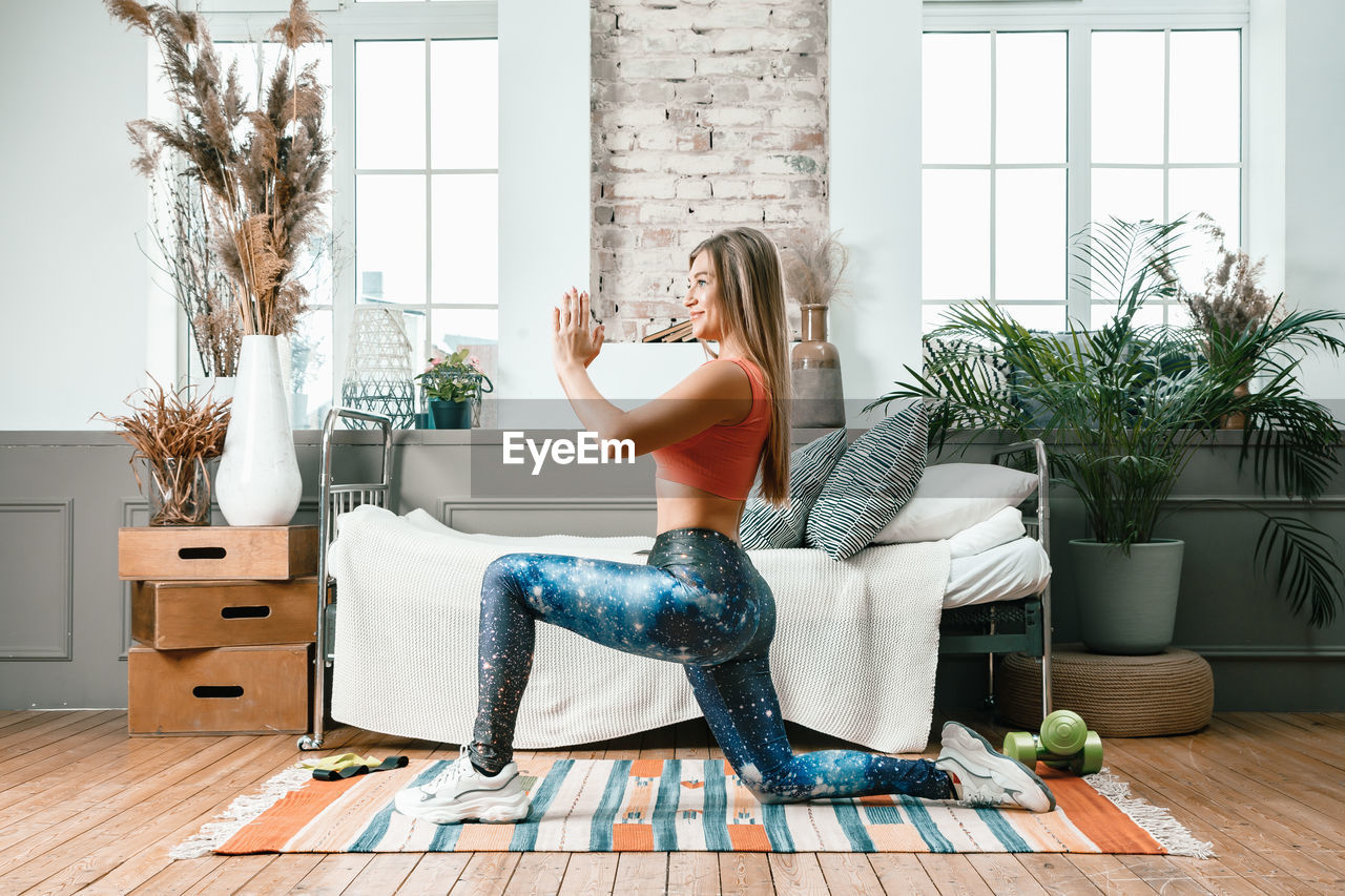 A cheerful athlete with blond hair lunges in the bedroom with online