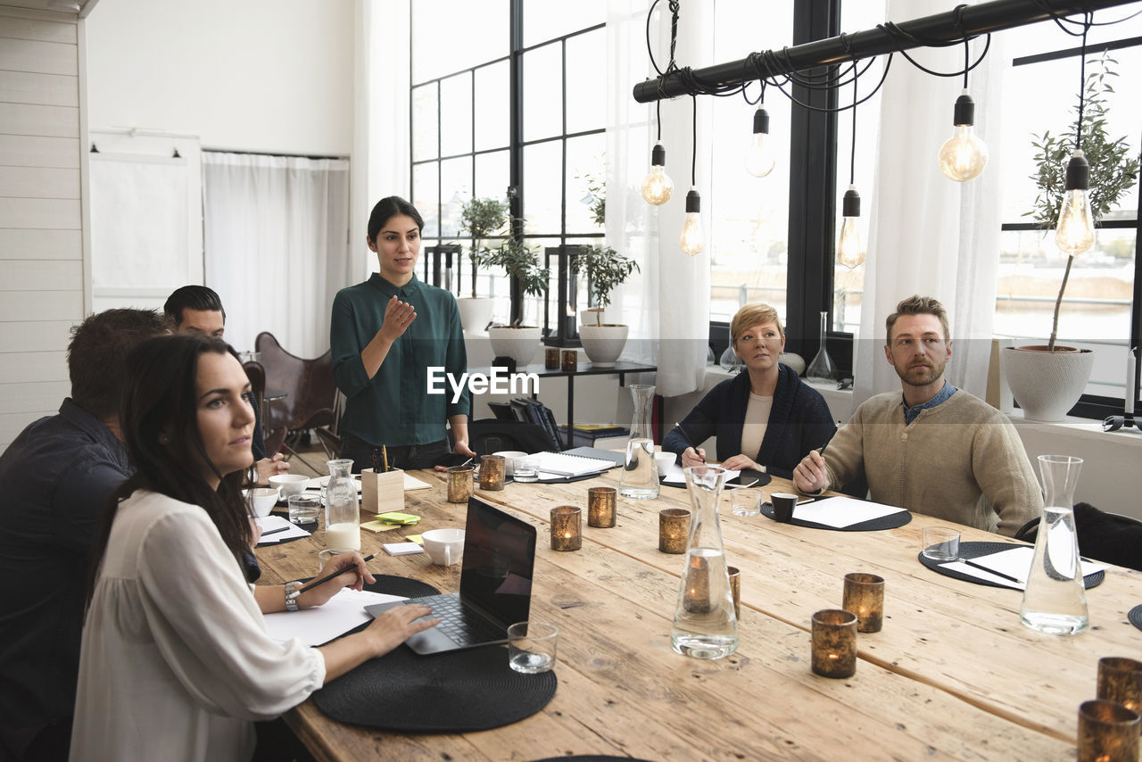 Businesswoman explaining to colleagues during meeting at table in office