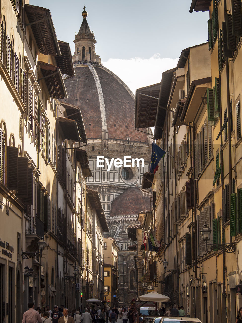 People walking on street leading towards florence cathedral against sky