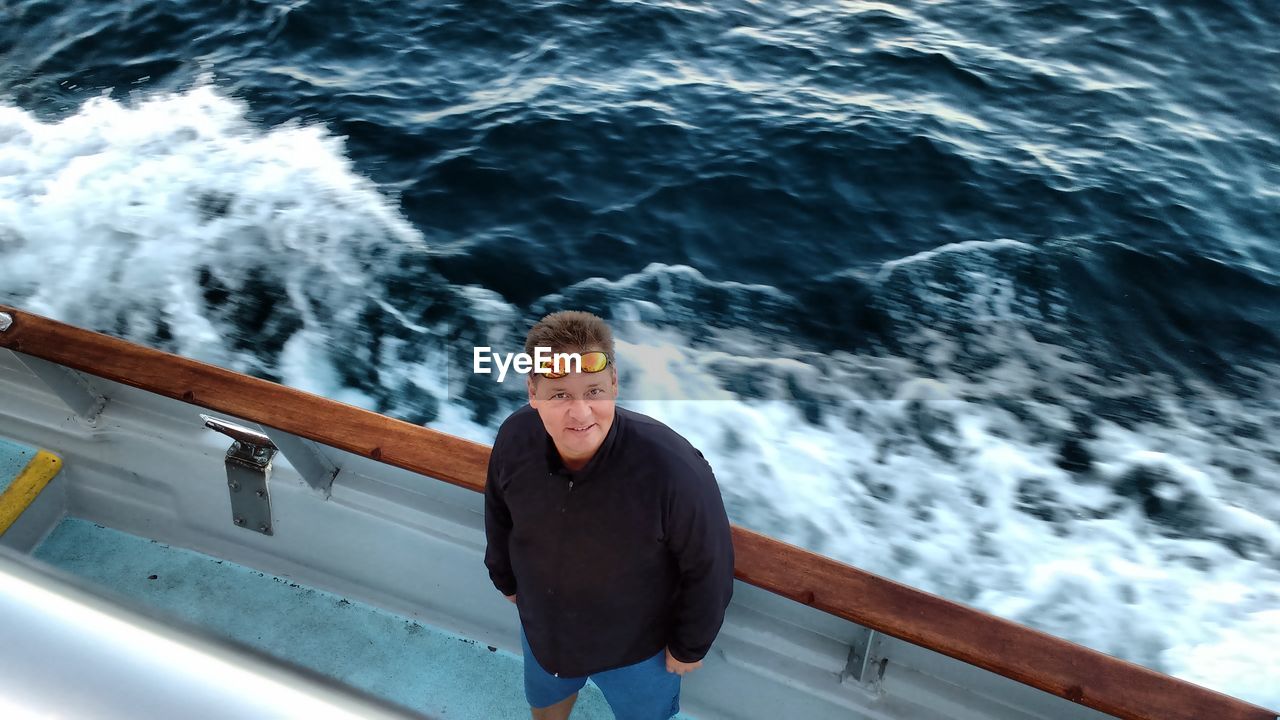 High angle portrait of man standing at sailboat