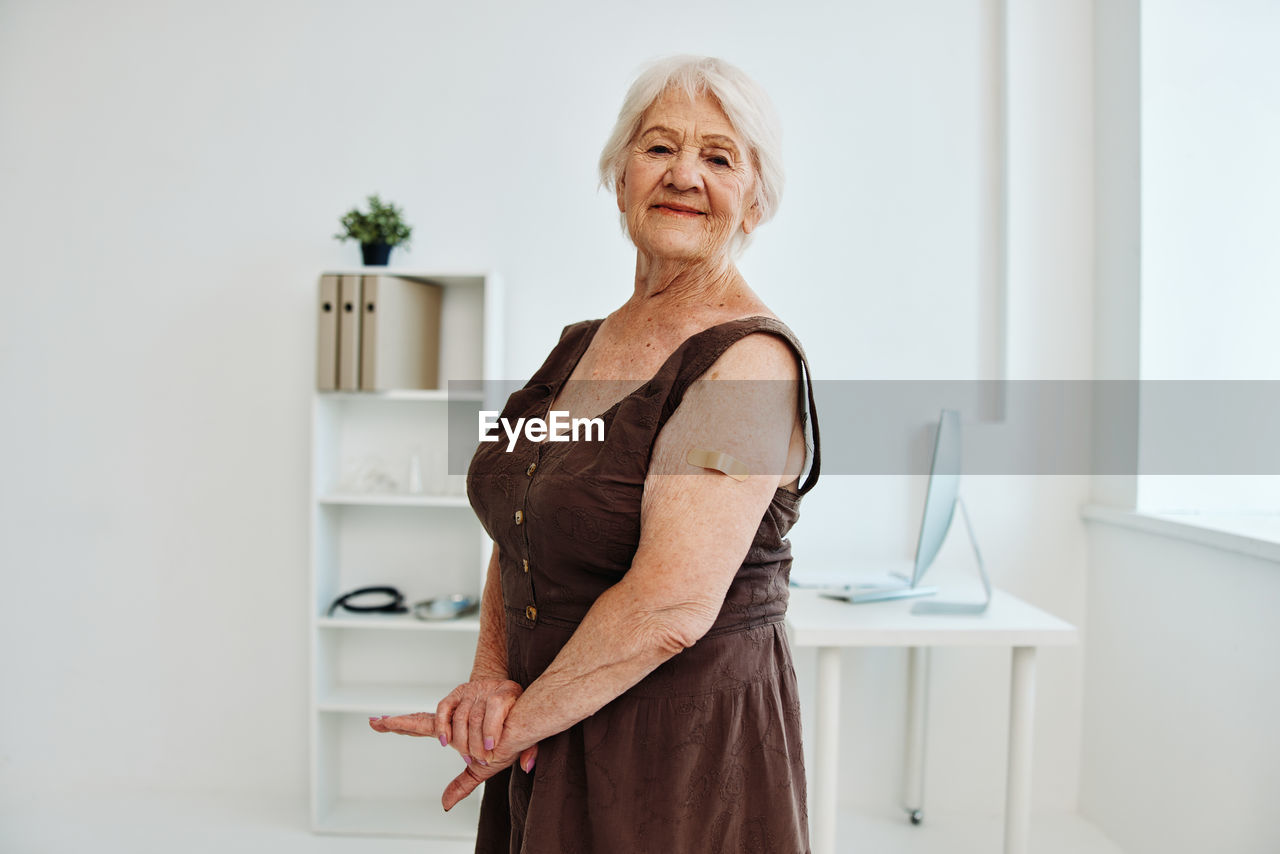 PORTRAIT OF SMILING WOMAN STANDING AGAINST WALL AT HOME