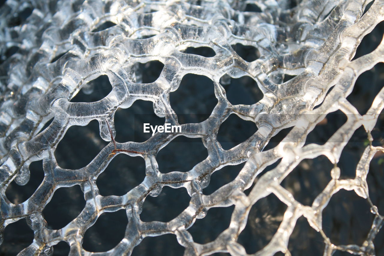 Close up of frozen ice in icicles and hexagon patterns on metal wire cover the frost on garden pond