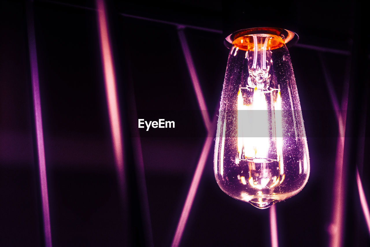 CLOSE-UP OF ILLUMINATED LIGHT BULBS HANGING AGAINST BLACK BACKGROUND