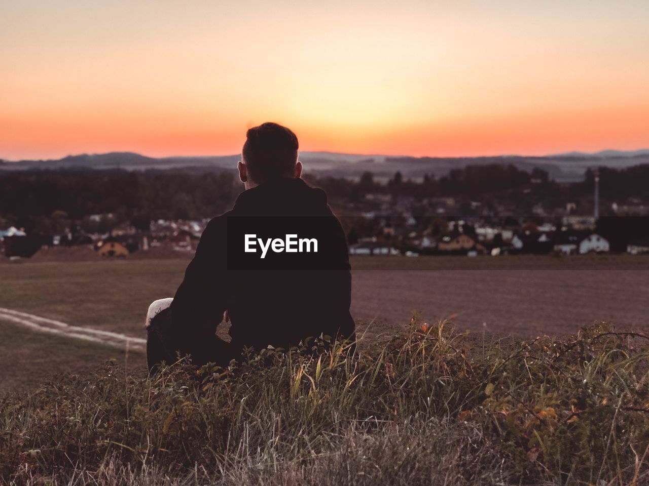 Rear view of man sitting on land during sunset