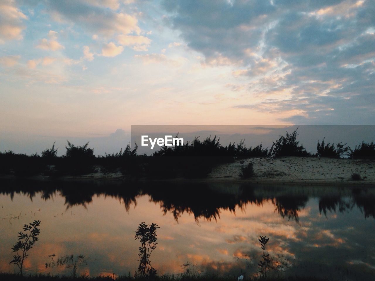 REFLECTION OF SILHOUETTE TREES ON LAKE AGAINST SKY