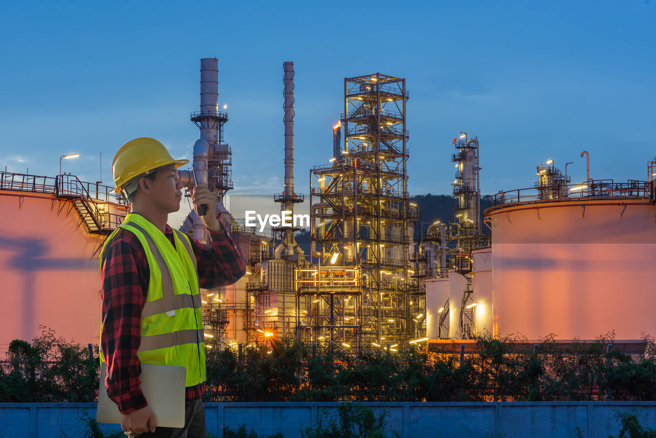 People standing at illuminated factory against sky at night