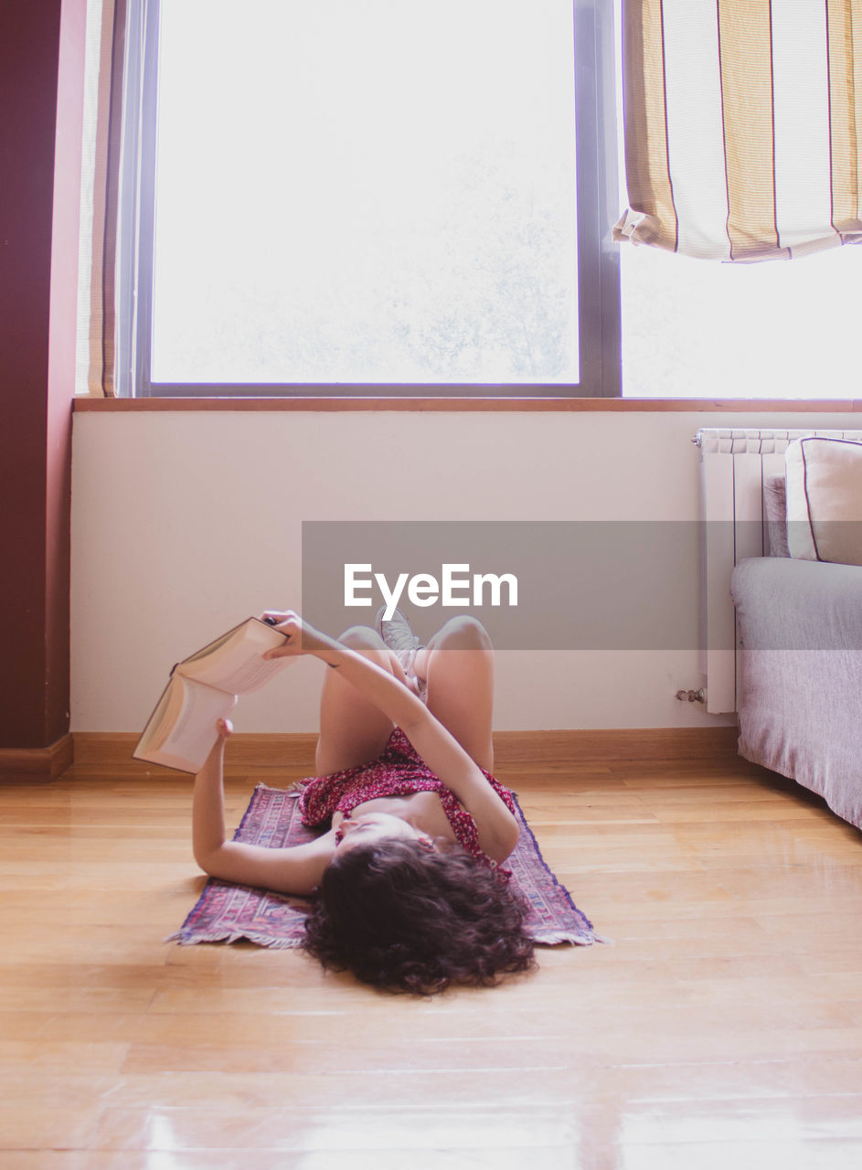 Young girl reading lying on a carpet with her feet up