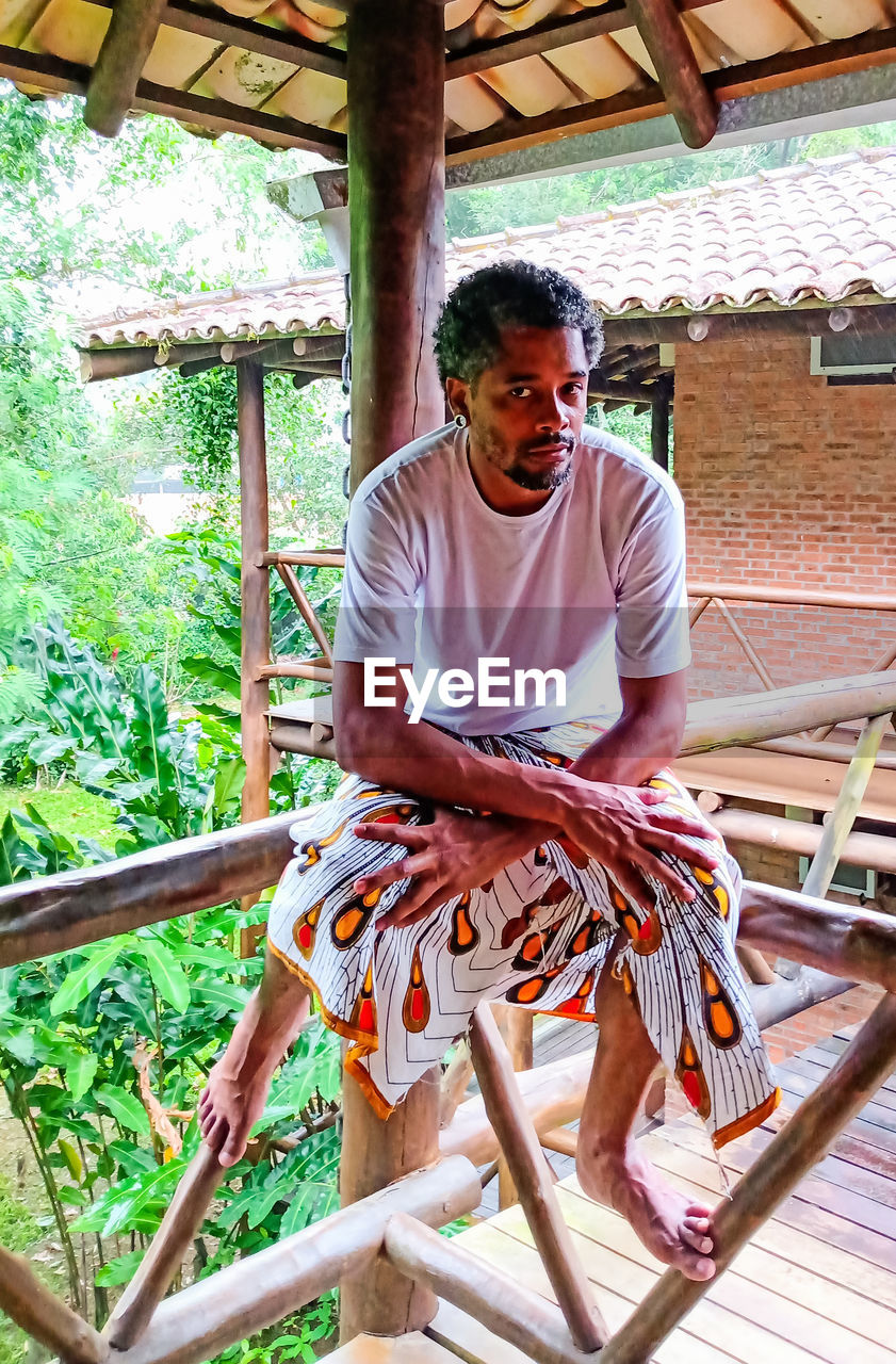 Portrait of man sitting on wooden railing outdoors