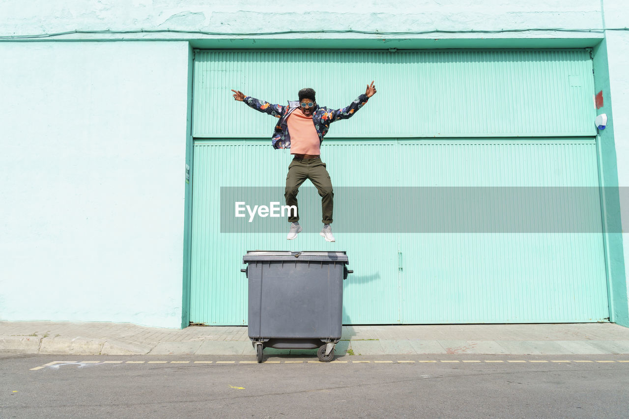 Carefree man jumping from garbage bin on sunny day