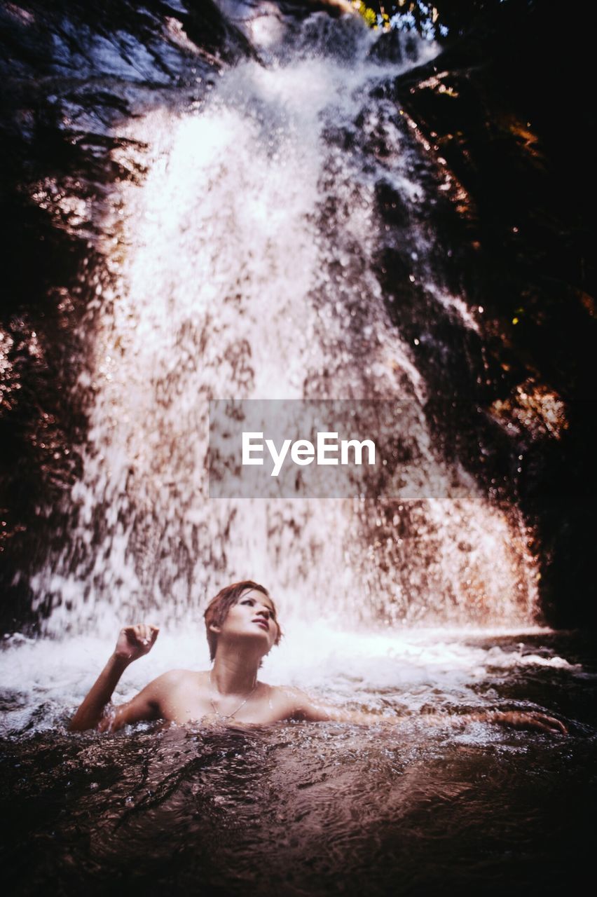 Shirtless woman swimming in river against waterfall