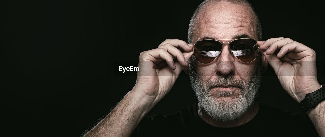 portrait of young man wearing sunglasses against black background