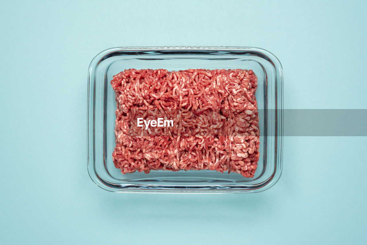 Above view with ground beef in a glass food container on a blue table. ground beef in a glass dish.