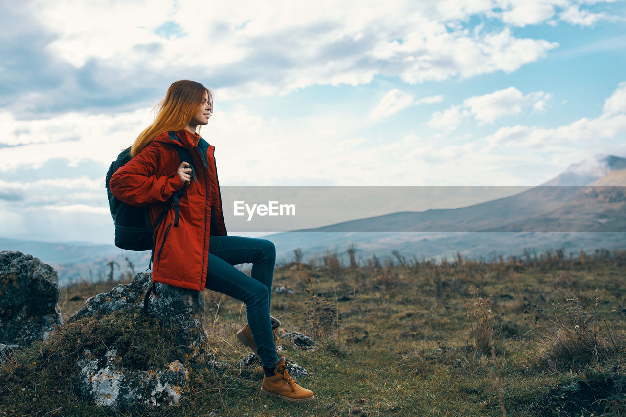 FULL LENGTH OF WOMAN SITTING AGAINST MOUNTAINS