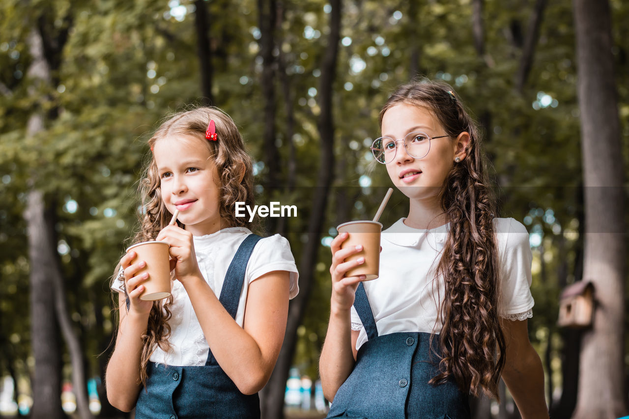 Two schoolgirls are drinking from eco-friendly cups and drinking straws in the park