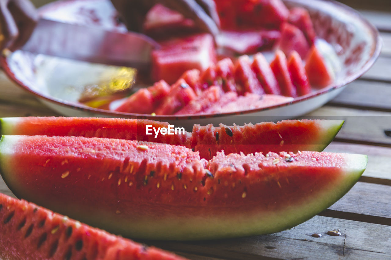 Close-up of man cutting watermelon slices on table