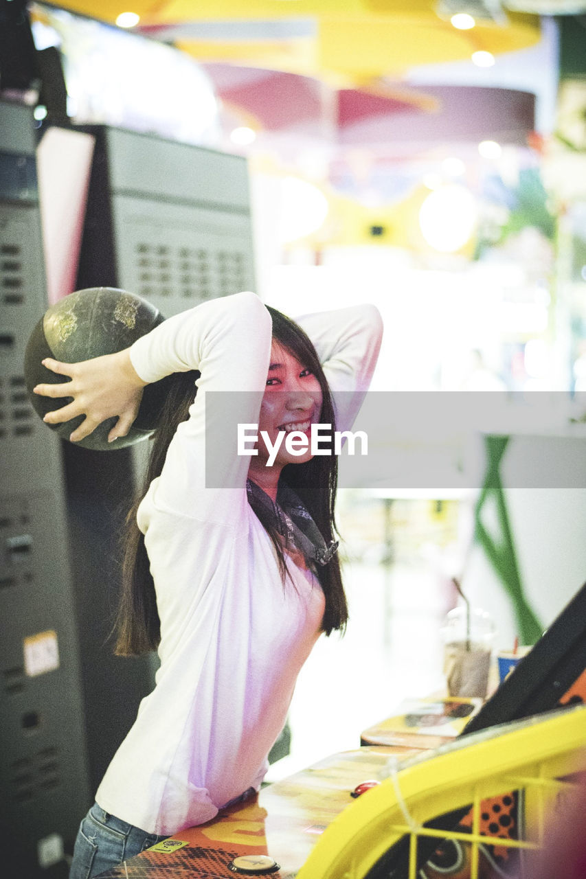 Cheerful young woman holding ball at amusement arcade