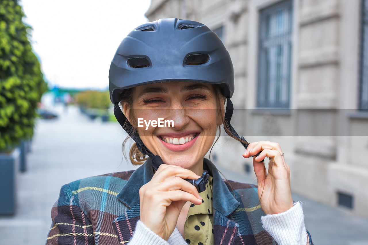 Portrait of young woman putting bicycle protective helmet