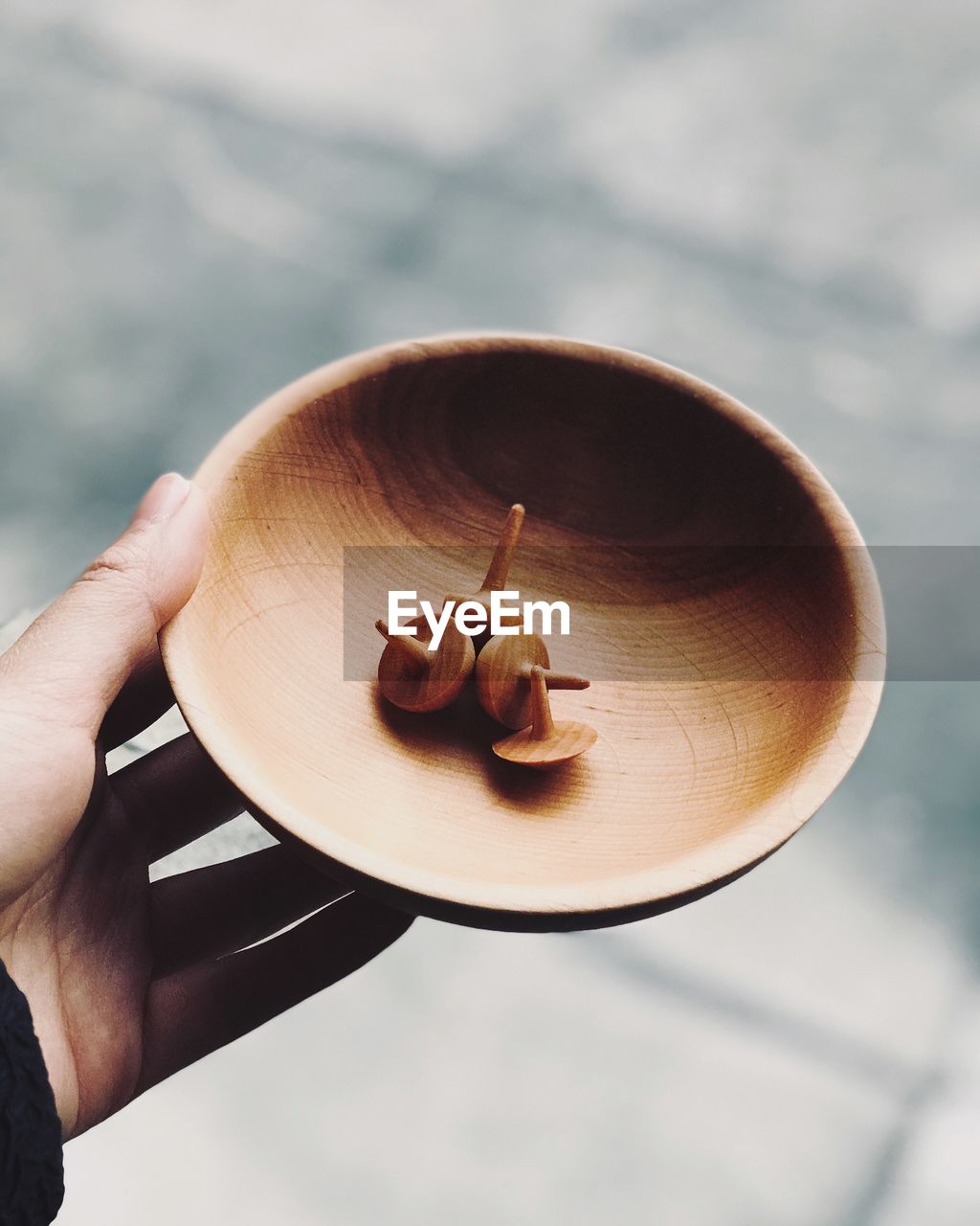 Cropped hand holding spinning tops in wooden bowl