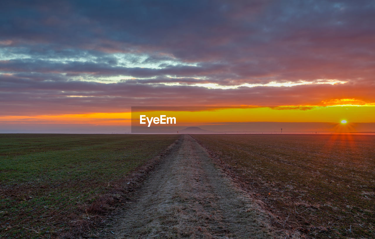 sky, horizon, cloud, sunset, landscape, environment, beauty in nature, scenics - nature, nature, field, land, sunlight, tranquility, tranquil scene, dawn, the way forward, dramatic sky, diminishing perspective, no people, vanishing point, prairie, horizon over land, evening, road, rural scene, sun, sea, plain, idyllic, orange color, transportation, outdoors, plant, non-urban scene, urban skyline, cloudscape, hill, agriculture, grass, afterglow, coast, rural area, travel, water, moody sky, footpath