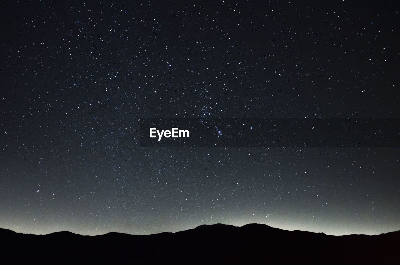 LOW ANGLE VIEW OF SILHOUETTE MOUNTAIN AGAINST STAR FIELD