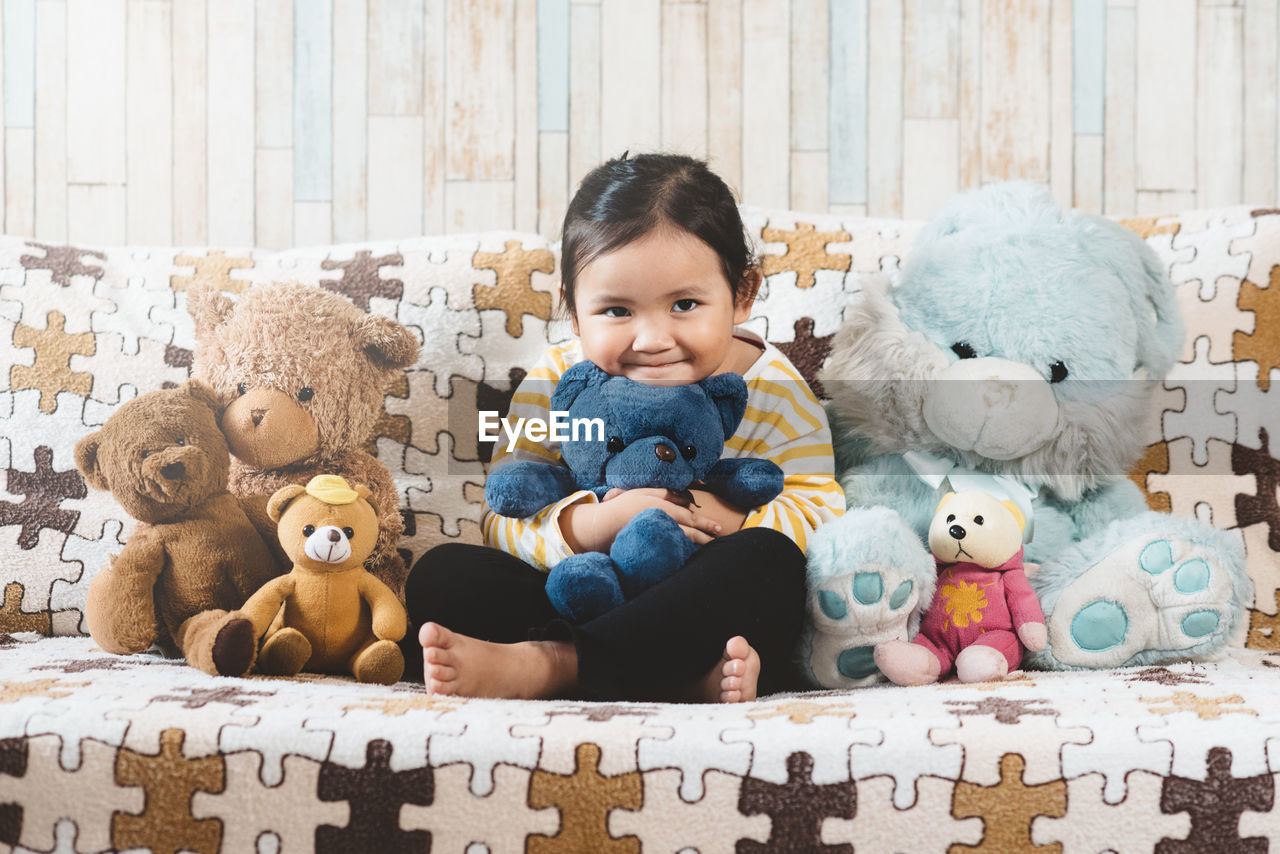 Portrait of girl sitting with teddy bears on sofa at home