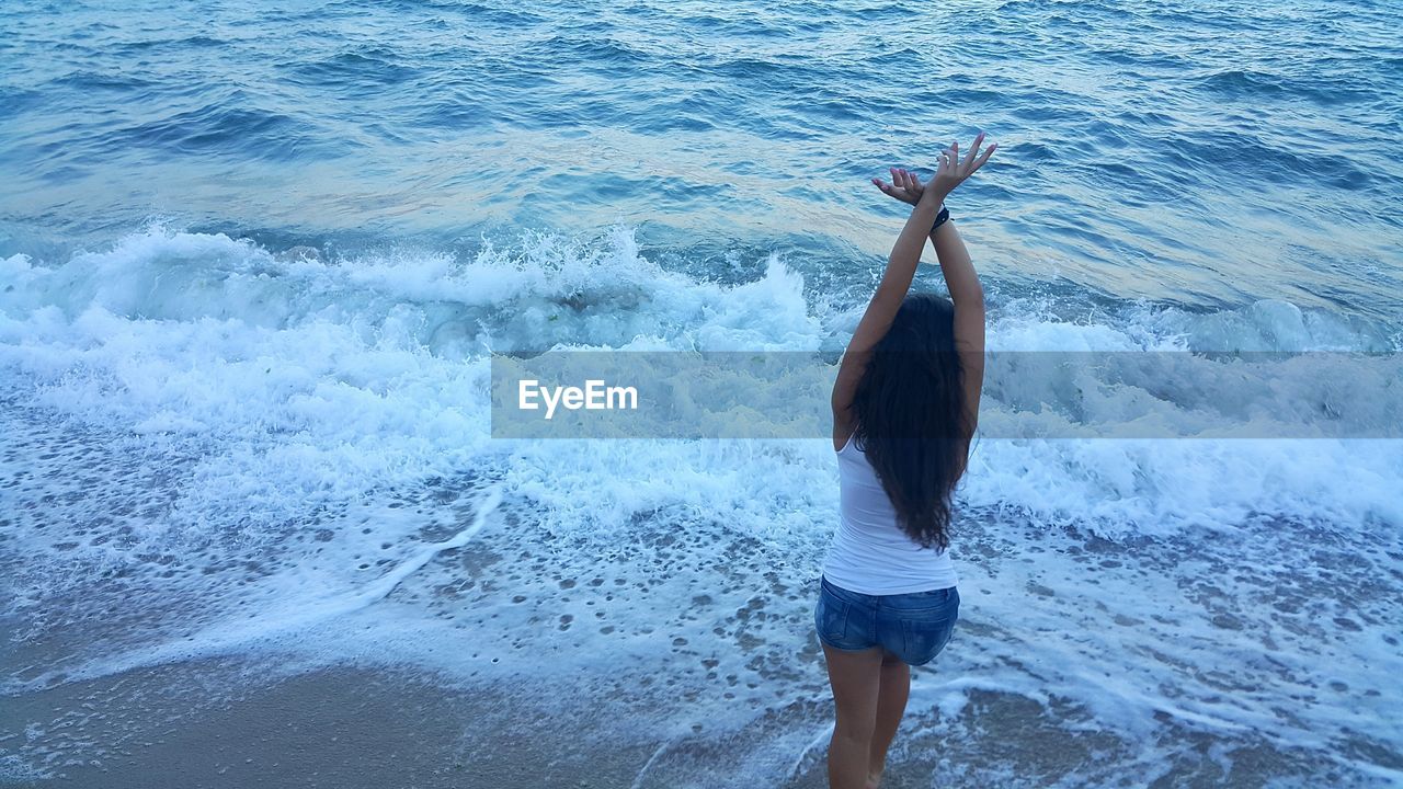 High angle view of woman with arms raised standing in sea