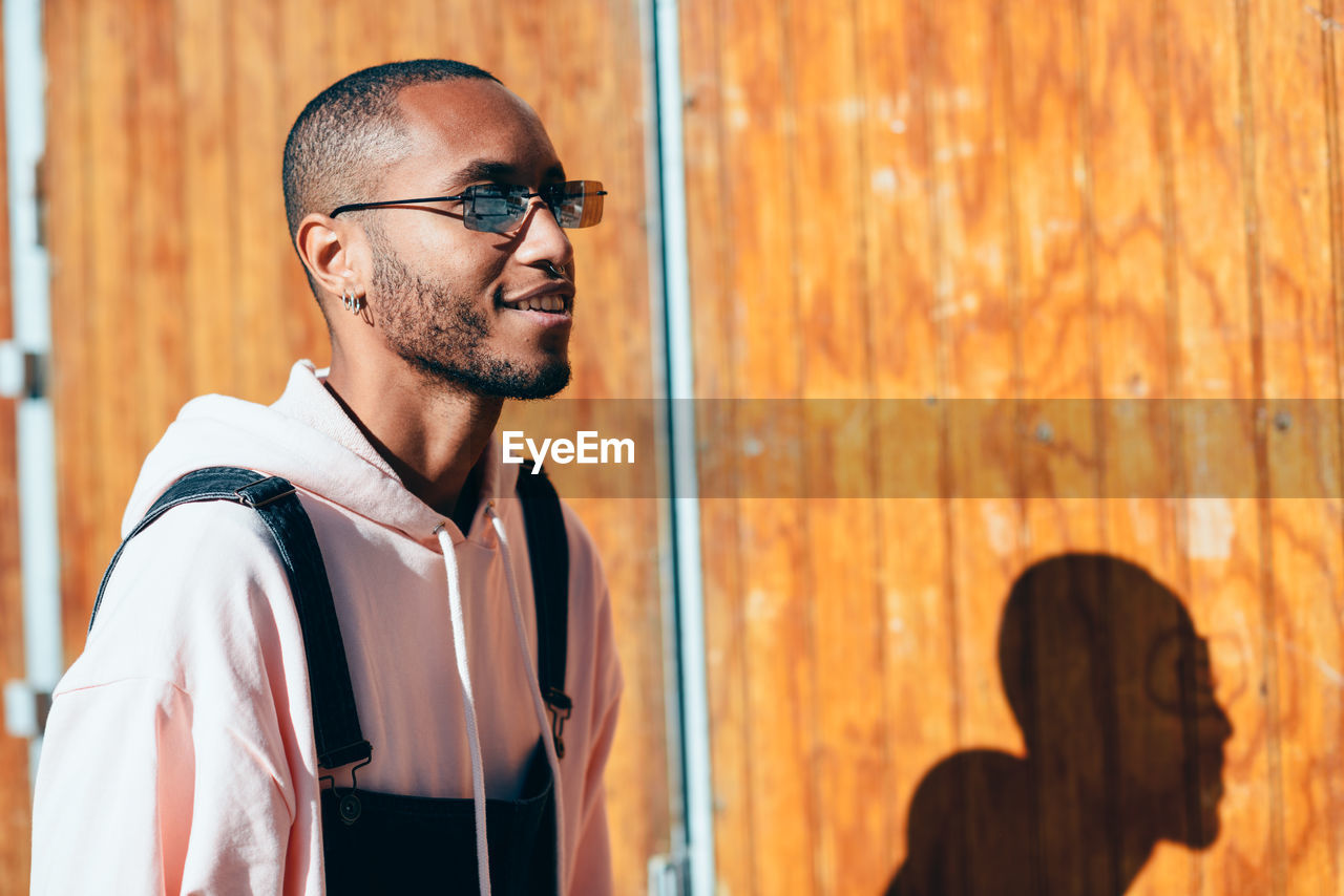 Smiling man wearing sunglasses while standing against wall