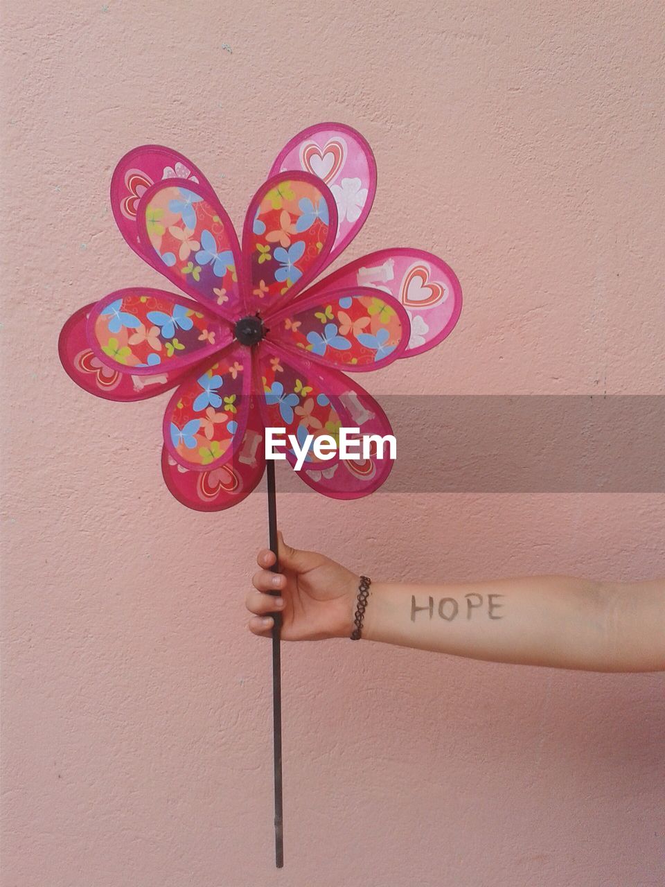 Cropped hand of girl with hope text holding pinwheel against wall
