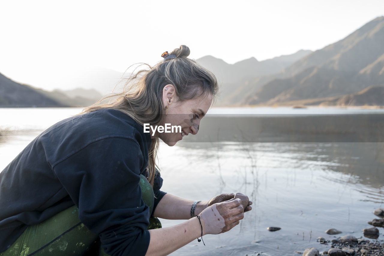 Woman putting mud on hands and face while enjoying outdoors in nature.