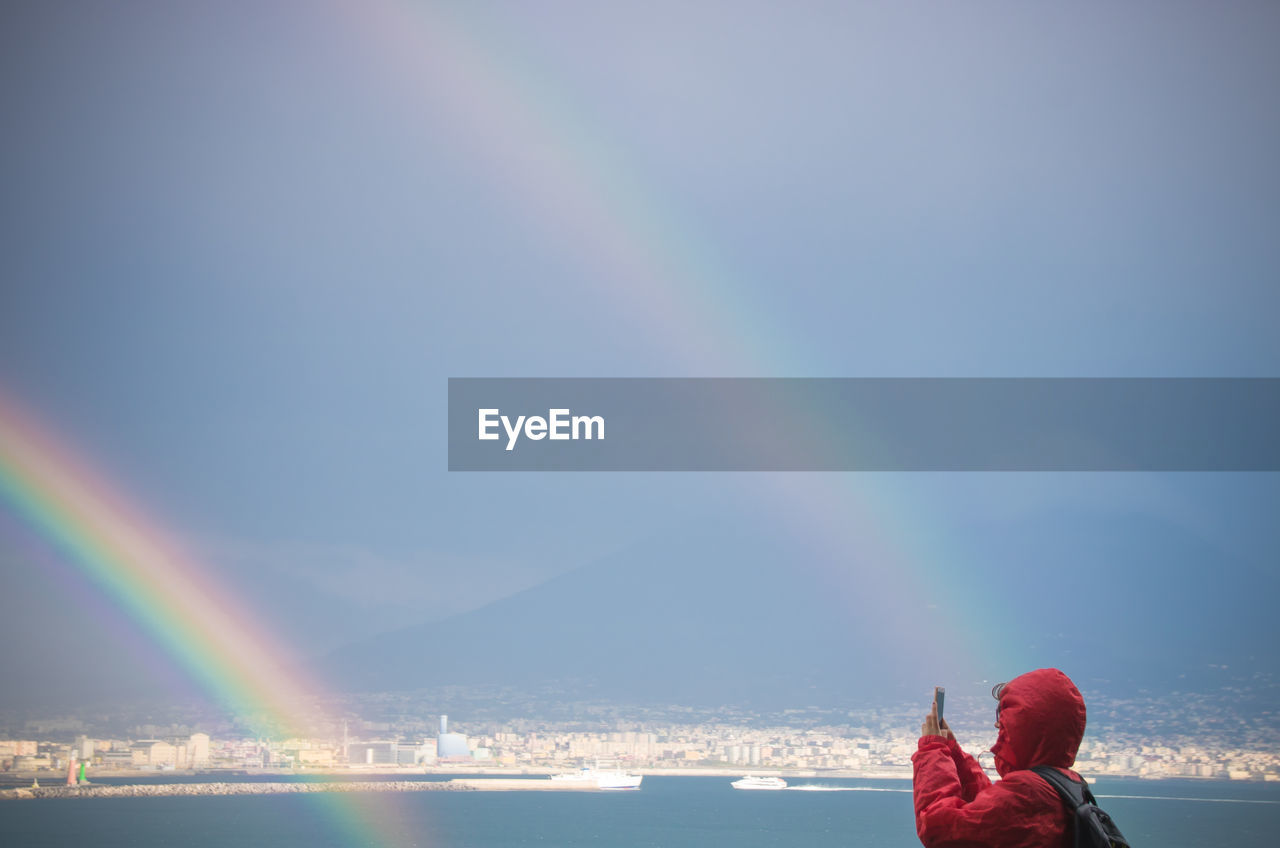 Woman photographing double rainbow and lake