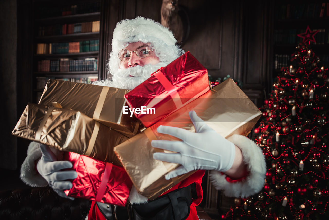 Portrait of santa clause holding gift by christmas tree at home