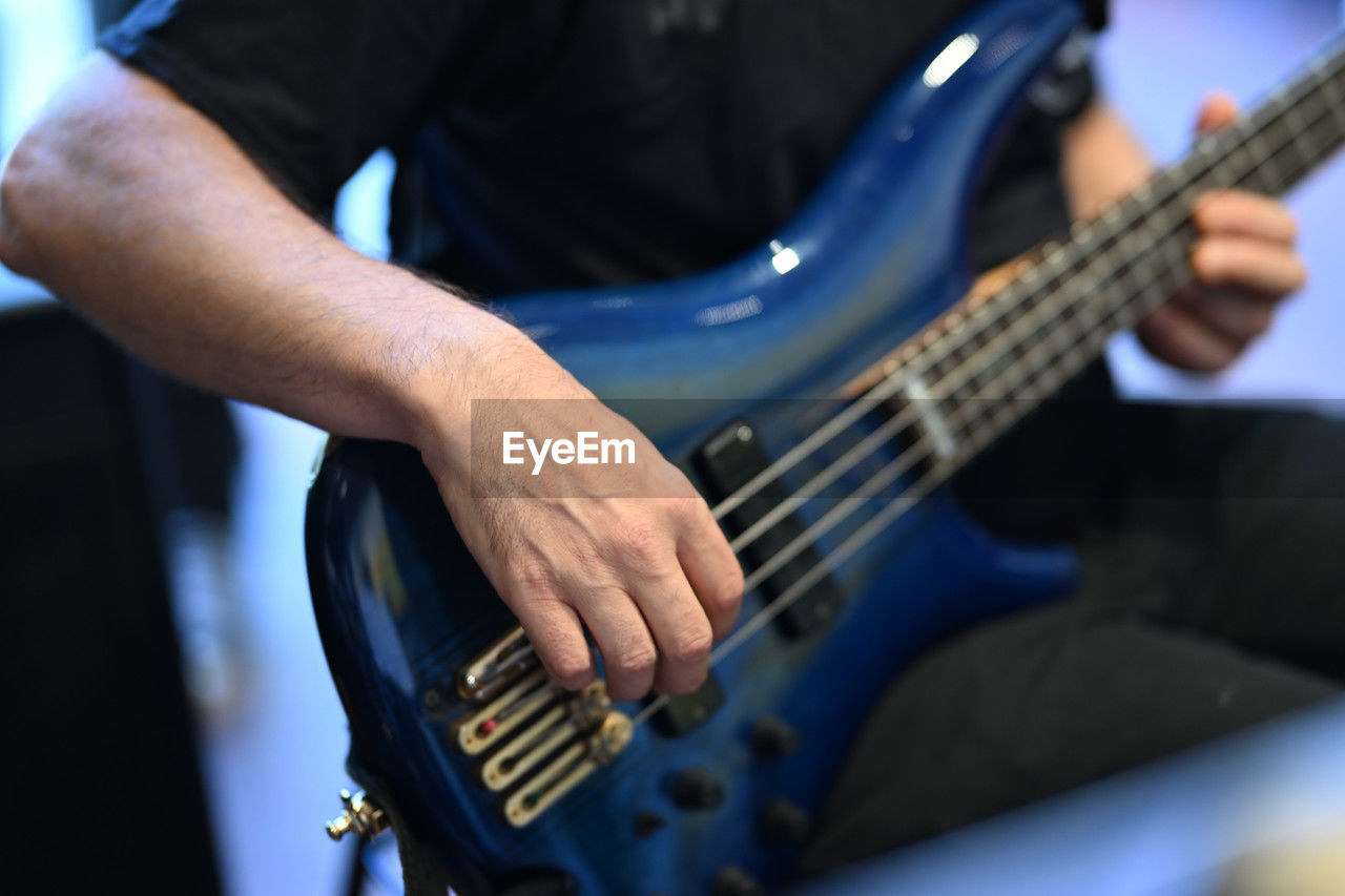 musical instrument, music, guitar, arts culture and entertainment, musician, string instrument, bass guitar, blue, one person, musical equipment, adult, plucking an instrument, men, electric guitar, skill, plucked string instruments, performance, midsection, hand, concert, occupation, indoors, focus on foreground, person, acoustic guitar, holding, rock music, close-up, young adult, casual clothing, selective focus, enjoyment