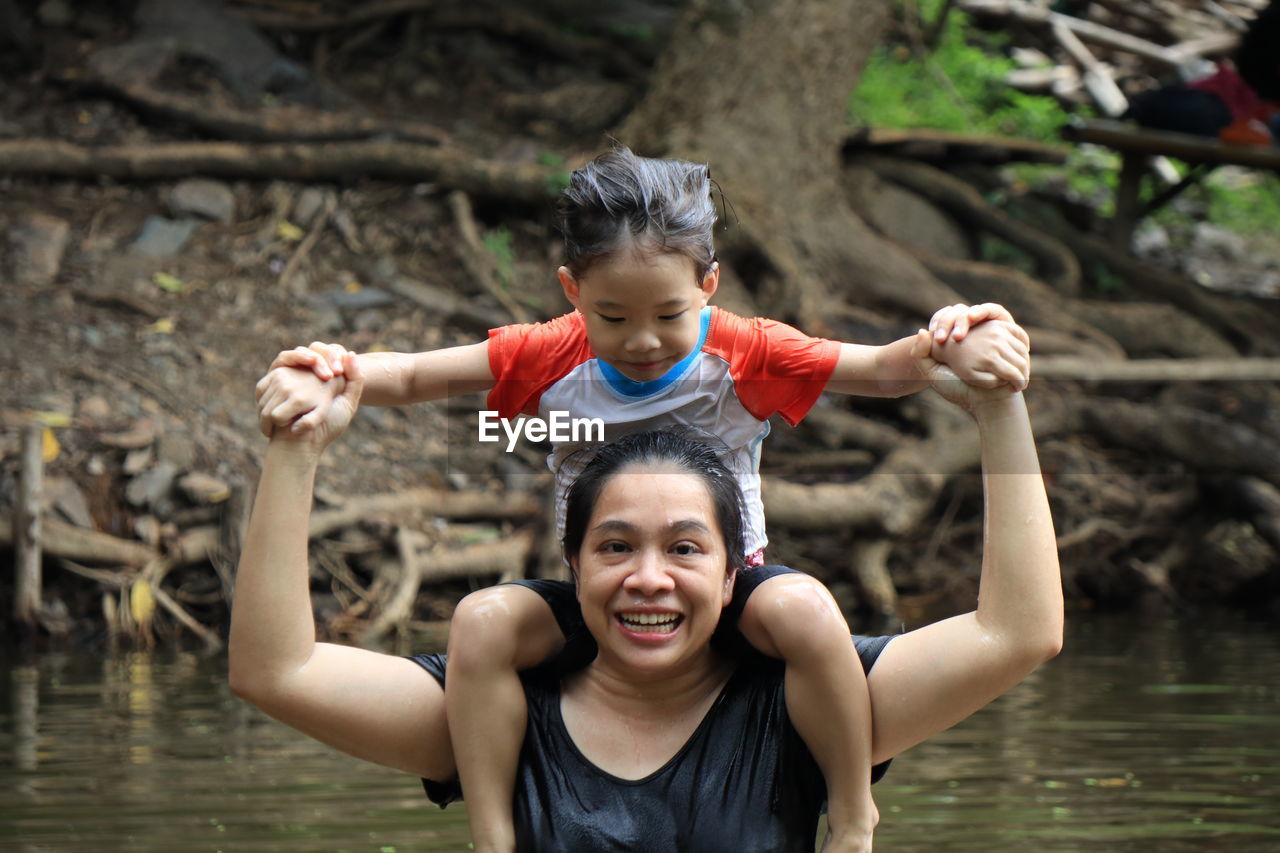 Portrait of cheerful mother carrying son on shoulders in river