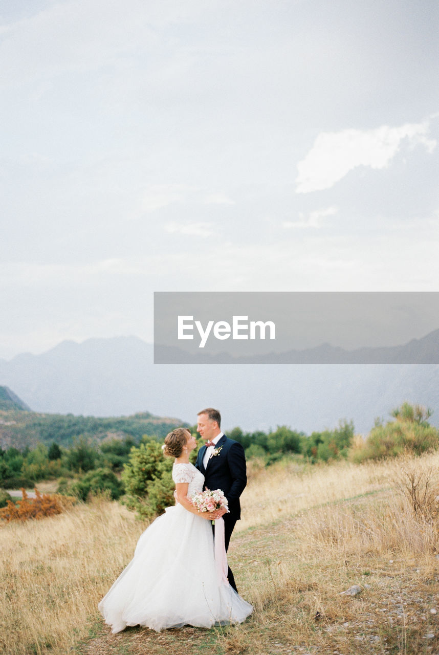 rear view of bride and bridegroom standing on field against sky