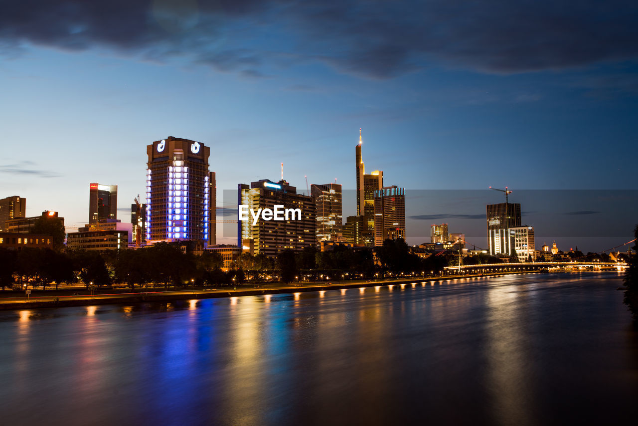 Illuminated buildings by river against sky in city in frankfurt, germany 