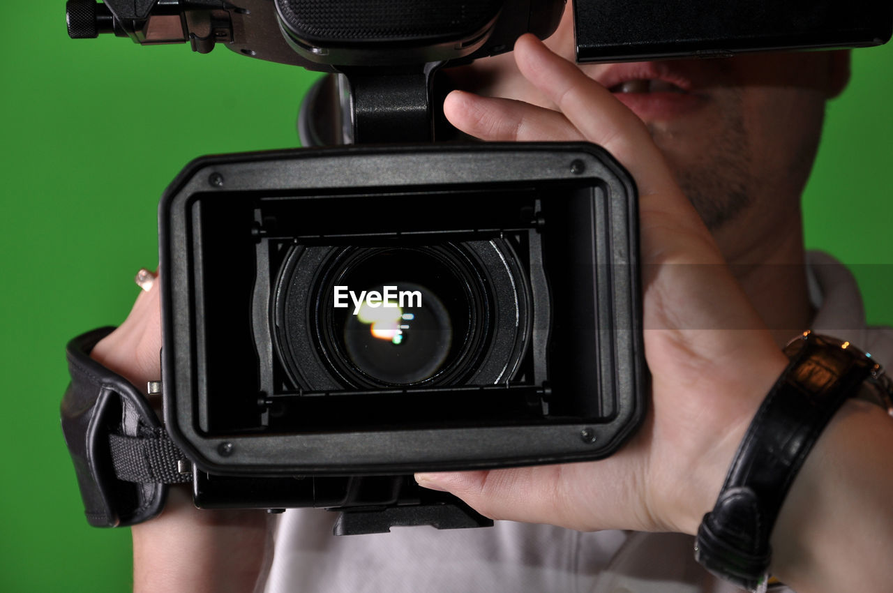 Close-up of man holding camera standing against green background