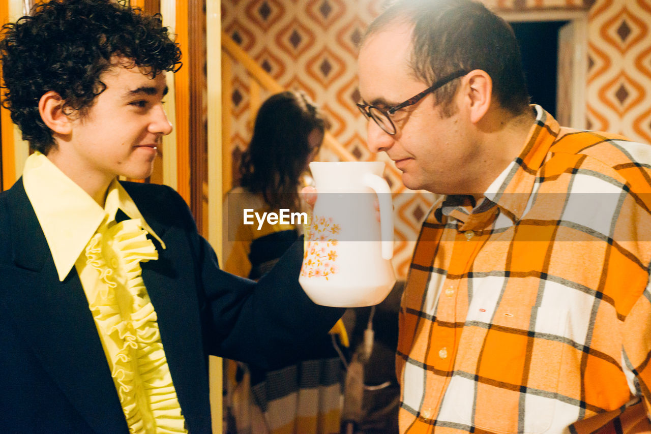 Father smelling jug held by son at home