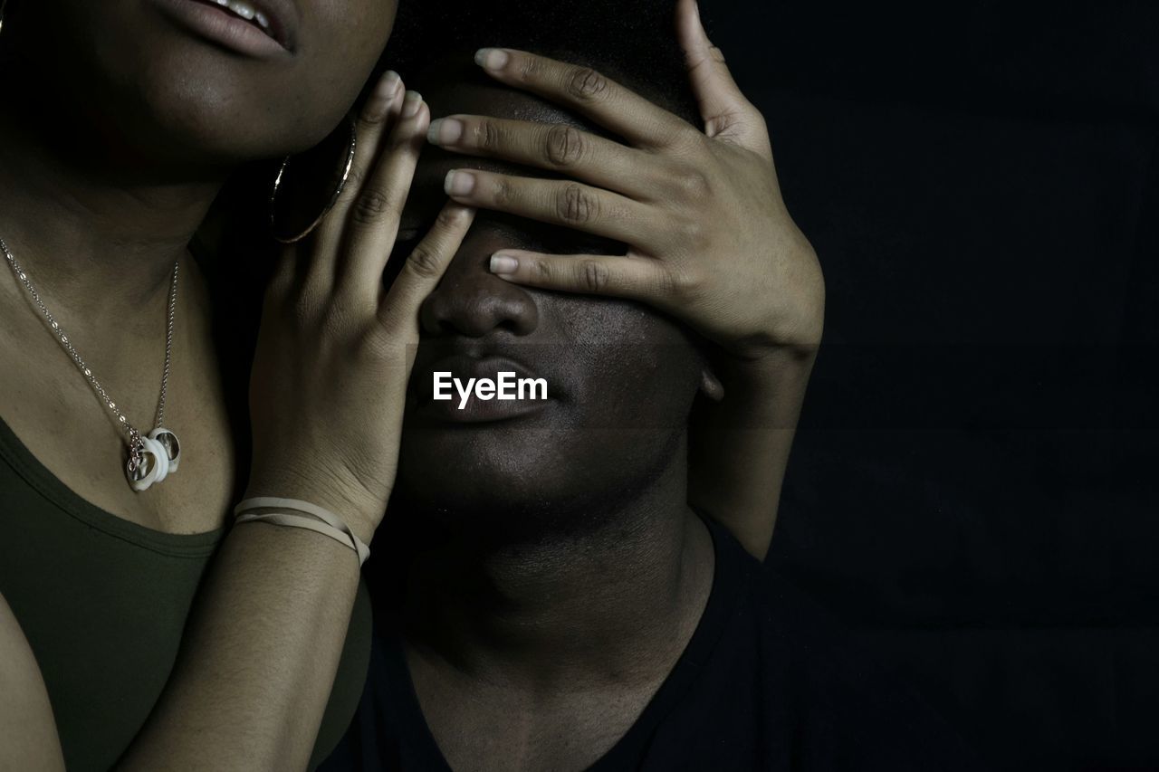 Woman covering eyes of man against black background