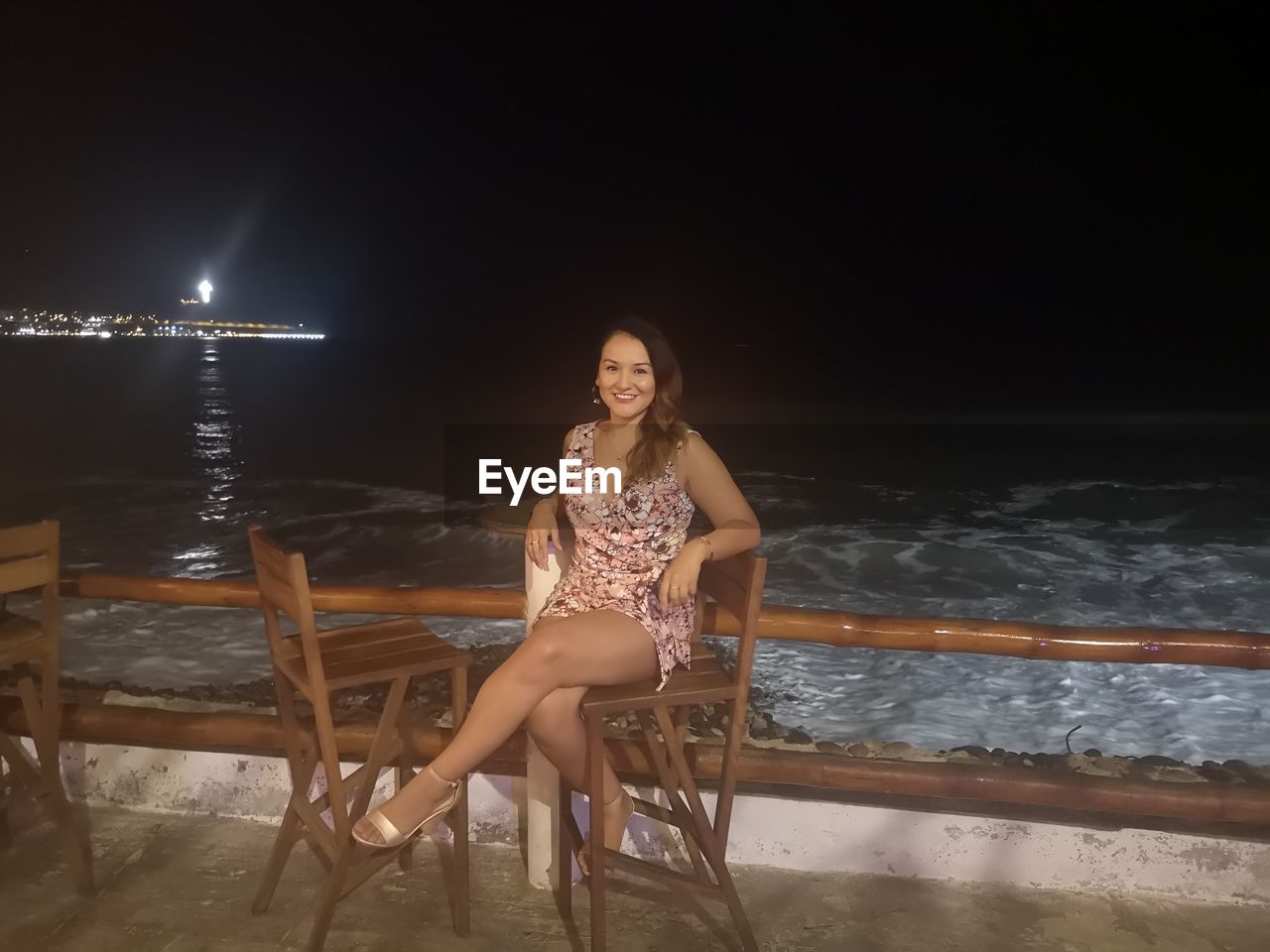 PORTRAIT OF WOMAN SITTING BY SEA AGAINST SKY