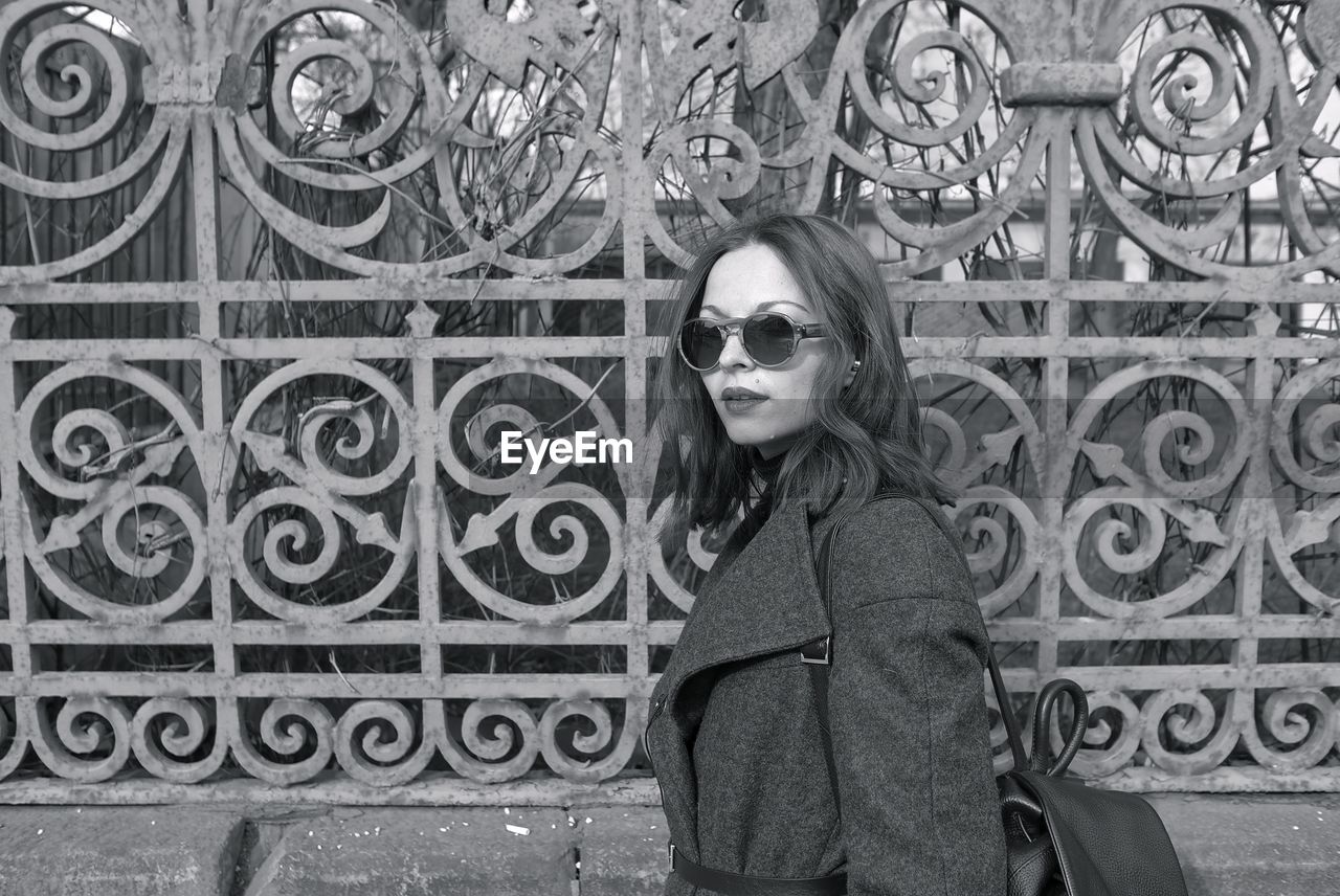 Side view close-up of woman wearing sunglasses while standing by fence