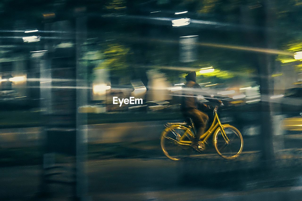 BLURRED MOTION OF YELLOW BICYCLE ON ROAD AT NIGHT