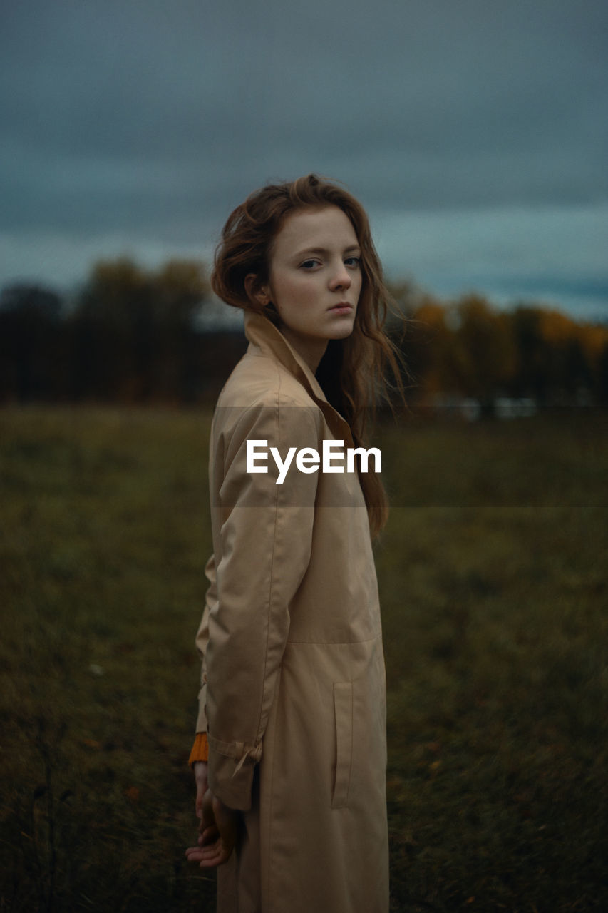 YOUNG WOMAN LOOKING AWAY WHILE STANDING ON LAND