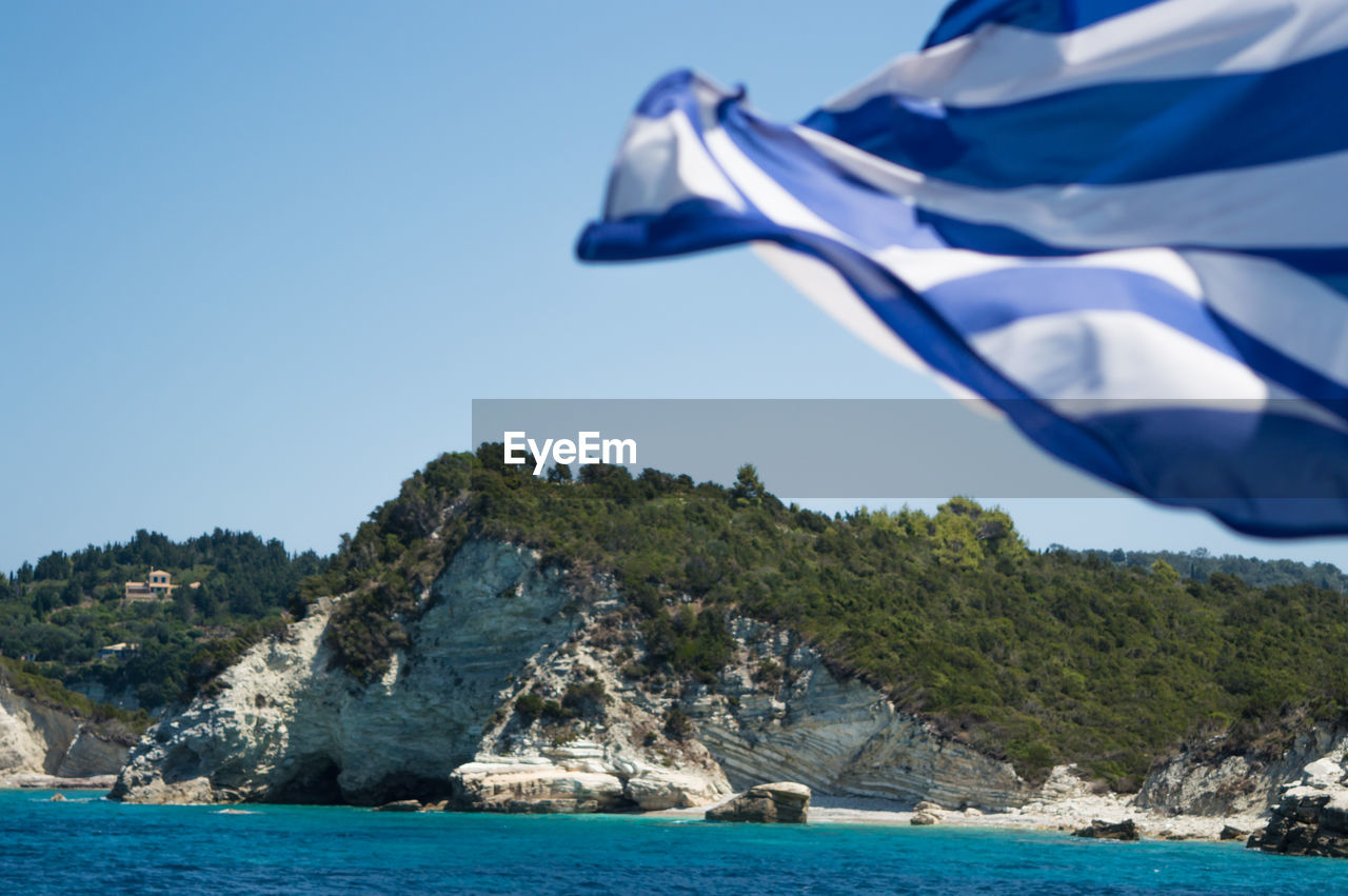 Greek flag waving against rocky mountain by sea