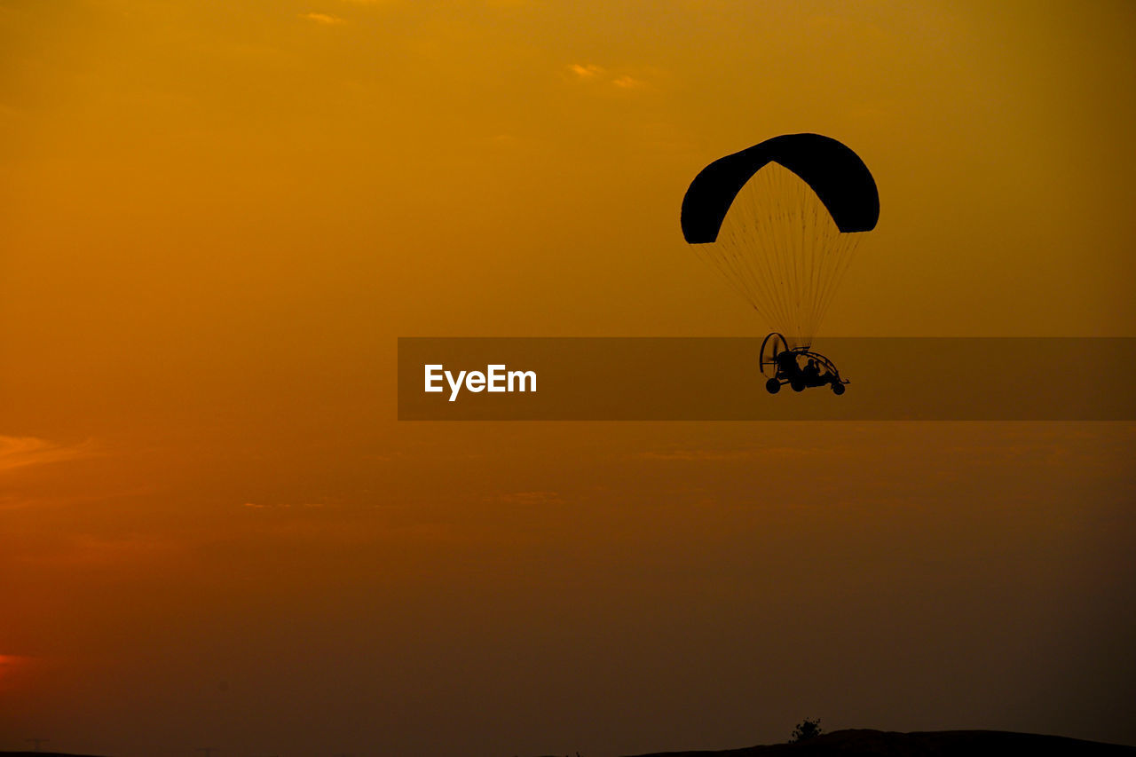 low angle view of people paragliding against sky during sunset
