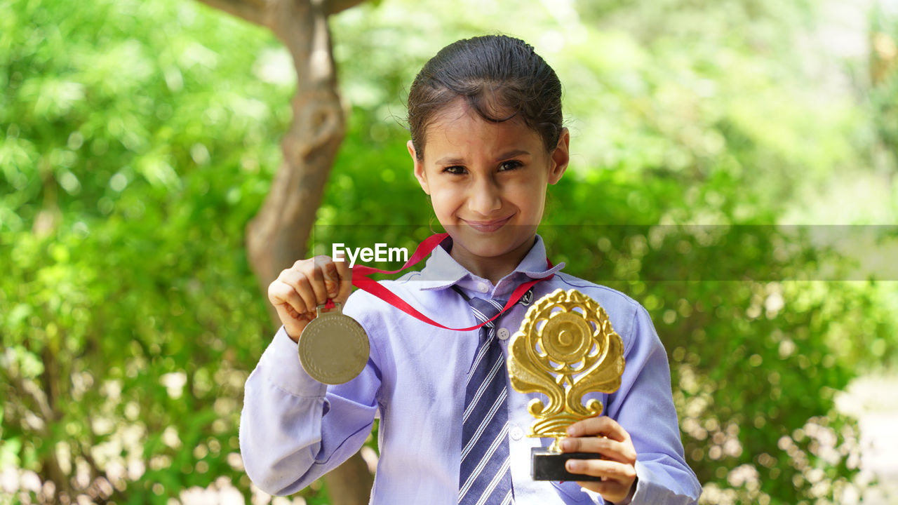 Portrait of a happy school girl wearing school uniform celebrating victory trophy in hand. 