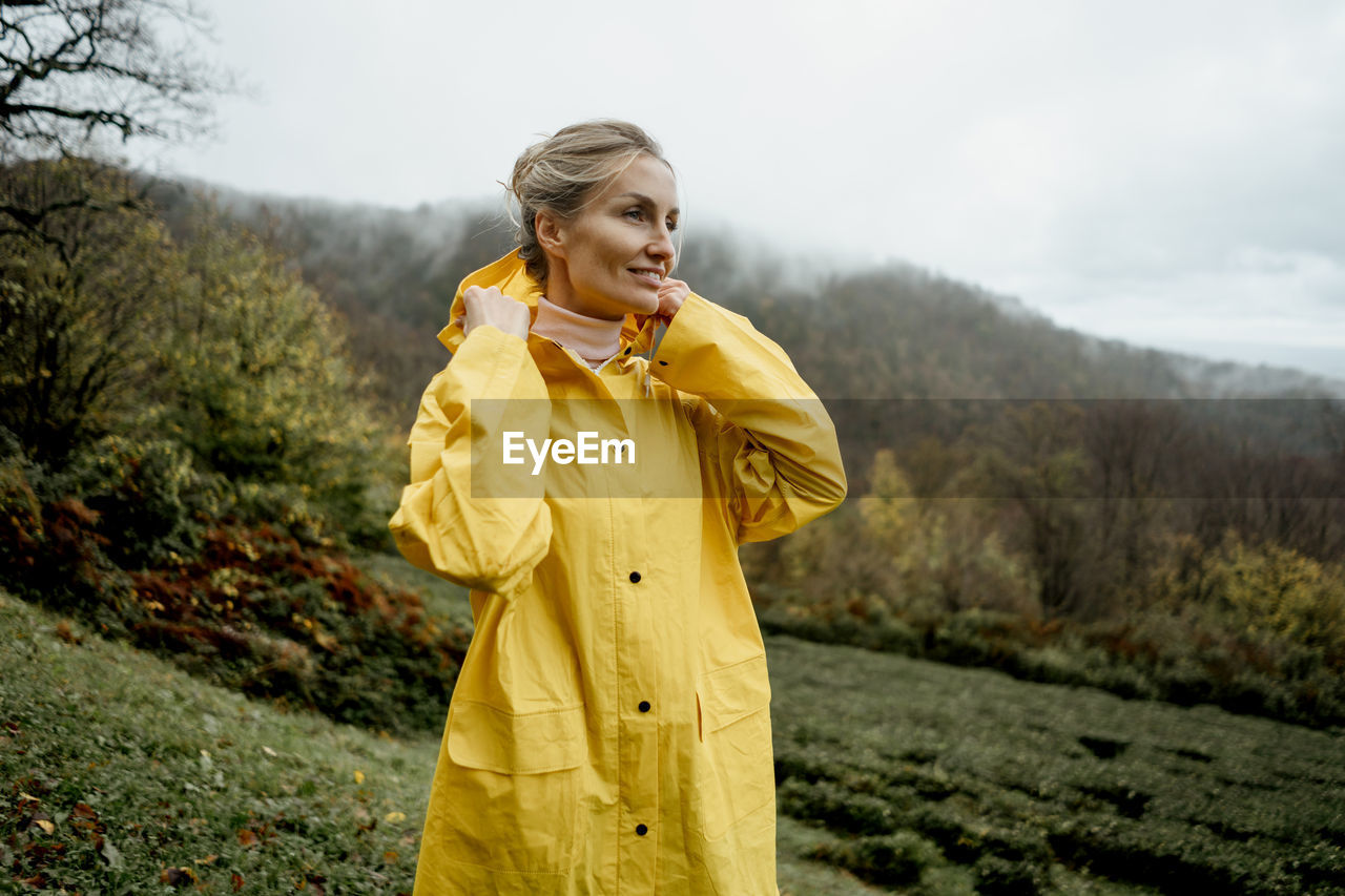 Pretty woman in yellow raincoat walking in rainy weather in the countryside